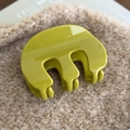 Détail d'une pince à cheveux en acrylique vert brillant sur un tissu beige doux - Vert