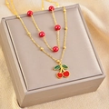 Primo piano della collana con ciondolo a ciliegia dorata e perle rosse su portagioie grigio - Collana di Ciliegie in Smalto