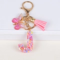 Macro detail of initial J keychain featuring pink tassel, resin butterfly and star sequins - Letter J