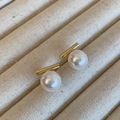 Elegante goldene Stabohrringe mit runden weißen Perlen in einer beigen Schmuckschatulle - Gold Weiß Glanzperle