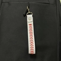 Mini white leather baseball keychain with red stitching on a black backpack - White