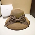 Foldable wide brim straw hat in light brown with a large dark brown satin ribbon bow - One Size (Adjustable 55-58.5cm) / Coffee Bow / [product Attributes] This Product Is A Retro-style [sun Hat] Primarily In A Natural [light Brown/camel] Color With A Wide And Flat Brim. A Large [dark Brown Satin Ribbon Bow] Adorns The Side Of The Hat. The Material Features A Tightly Woven [herbal] Texture Giving It An Elegant And Fashionable Overall Style. [visual Presentation] Shot In A Simple Indoor Scene With Soft And Even Lighting Perfectly Highlighting The Texture And Details Of The Straw Weave. The Image Resolution Is Extremely High With A Clean And Noise-free Picture Rated [high] In Quality. The Composition Is Balanced The Colors Harmonious Showcasing A High Level Of Aesthetic Appeal. [text Content] Ocr Detected A Single Letter [d] Printed On The White Gift Box In The Left Background. Apart From This The Entire Image Contains No Chinese Characters Logo Watermarks Or Certification Marks. [review Conclusion] Determined [passed]. The Image Content Is Healthy And Meets The Usage Standards Of Cross-border E-commerce Platforms Requiring No Removal Or Translation Processing. [logistics Label] Determined [none] Classifying It As A General Clothing And Accessories Product. [infringement Risk] Determined As [none]. Although The Background Box Has Letter Markings It Is Not Considered An Infringement Basis As A Photography Prop. The Main Product A Straw Hat Does Not Display Any Brand Trademarks Or Classic Protected Designs. The Probability Of Infringement Is [0.1]. [product Parameters] Key Parameters Include: [straw Material] [two-tone (light Brown/dark Brown)] [wide Brim Design] [bow Decoration].