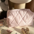 Dettaglio trousse trapuntata a quadretti rosa con cerniera su tavolo bianco con accessori - Rosa