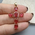 Close-up of gold cross pendant with red gemstones and pink crystal accents held by hand - Red