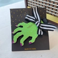 Glittery green zombie hand hair clip with purple tips and a striped bow on card - Green Hand