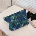 Dettaglio di pochette cosmetica in jacquard floreale blu e verde su tavolo. - Base Nera con Fiori Verdi e Blu