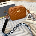 Detail of tan quilted crossbody bag with stylish patterned strap on white carpet - Brown