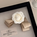 Detail van witte camellia stoffen bloem en champagne satijnen strik op een haarspeldje - Beige Camelia Strik Haarklem