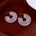 Detail of silver C-shape hoop earrings with embossed circular dot texture on dark fabric - Silver