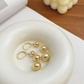 Vue détaillée de boucles d'oreilles boules dorées sur un plateau en céramique blanche - Pendentif Triple Boule Doré