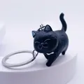 Close-up of black resin cat keychain with silver metal ring on white stand - Black