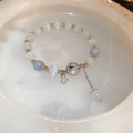 Detail of beaded bracelet with white cat-eye stones, blue beads, and star charms in a ceramic dish - Cat's Eye Beaded Star Bracelet