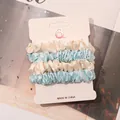 Close-up of four satin scrunchies in cream and sky blue on a display card for hairstyling - Off-White and Sky Blue