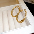 Close-up van gedraaide gouden oorringen op een wit fluwelen sieradendoosje - Goud