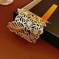Golden open cuff bracelet with vintage hollow flower design on a jewelry box - Gold