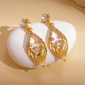 Orecchini a foglia dorati con strass su un ciottolo bianco con luce calda - Oro