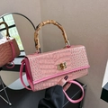 Detail of pink croc-embossed handbag featuring a unique bamboo handle and gold twist lock - Pink