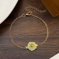 Detail of a gold-plated bracelet featuring a delicate green flower pendant on wood - Gold Green Resin Flower