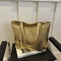 Golden tote bag with crocodile embossing texture and slim shoulder straps on a chair - Gold