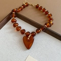 Macro view of amber acrylic heart pendant necklace in warm tones on a wooden tray - Necklace / Brown