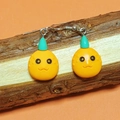 Close-up of handmade cartoon pumpkin earrings hanging on a natural wood stand - Orange