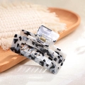 Detail view of square black and white tortoiseshell acetate hair claw on wooden tray - Cow Pattern