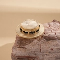 Detailed close-up of golden boater hat brooch with woven straw texture and black chain link - Gold