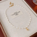 Detail van de kralenketting met een gouden schelphanger op een zacht linnen doosje - Ketting-Wit-Schelp