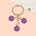 Cute gold metal keychain featuring three small dark purple daisy flower pendants - Purple