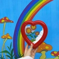 Close-up of a hand holding a red heart-shaped makeup mirror against artistic illustrations - Red