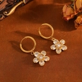 Gros plan de créoles dorées avec pendentifs fleurs en zircone étincelante sur fond vintage - Boucles d'Oreilles Fleur en Zircone Blanche Dorée