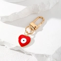 Detail von goldenem Herz-Schlüsselanhänger mit rotem Evil Eye auf weißem Stein - Rotes Herz