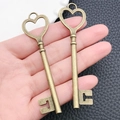 Primo piano di due ciondoli a chiave vintage in bronzo a forma di cuore tenuti in mano - Chiave a Cuore in Bronzo Antico 22x87mm