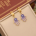 Gold Hamsa Hand earrings with blue evil eye detail in a stylish jewelry box - Earrings (Style 3)