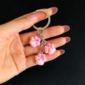 Detail of pink resin cat paw charms on a silver metal keychain held against black background - Pink White