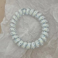 Macro view of white spiral phone cord hair tie with vibrant colorful linear patterns - Trendy Blue Dots