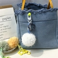 Detail of blue denim handbag featuring a white plush pompom and yellow leather handle - White