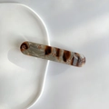 Detail view of marble-pattern hair clip with gold flower inlay on white ceramic plate - Brown Gray