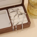 Silver bow tassel earrings on beige velvet lining inside a wooden jewelry box - Silver Earrings