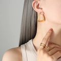 Elegantes pendientes geométricos en U bañados en oro y anillos minimalistas en una modelo - Dorado
