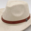 Detailed close-up of brown leather hat band with vintage metal emblem on felt cowboy hat - One Size / Brown Round