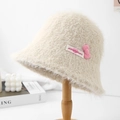 Detailed view of a fluffy cream bucket hat featuring a pink bow and decorative label - Beige