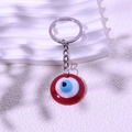 Roter Evil Eye Schlüsselanhänger mit silbernem Ring auf weiß gewelltem Hintergrund - Rot