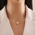 Gold circular pendant necklace with small metal beads on fine chain over beige blazer - Letter O