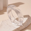 Makroaufnahme eines unregelmäßigen durchsichtigen Acryl-Armreifs auf einem weißen Naturstein - Weiß (Transparent)