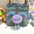 Close-up of purple plush monster keychain with blue horns on a denim bag - Purple