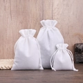 Three sizes of white linen drawstring jewelry bags displayed on a natural wooden background - Pure White