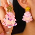 Macro shot of glitter star stud and pink acrylic Christmas tree cat pendant earrings - Pink Christmas Tree Cat
