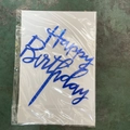 Blue acrylic Happy Birthday cake topper in protective packaging on a green surface - Sapphire Blue