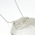 Minimalistische zilveren ketting met vierkante hanger op wit keramisch bord - Geometrisch Staal